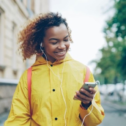 Mulher sorrindo ouvindo áudio no celular enquanto caminha